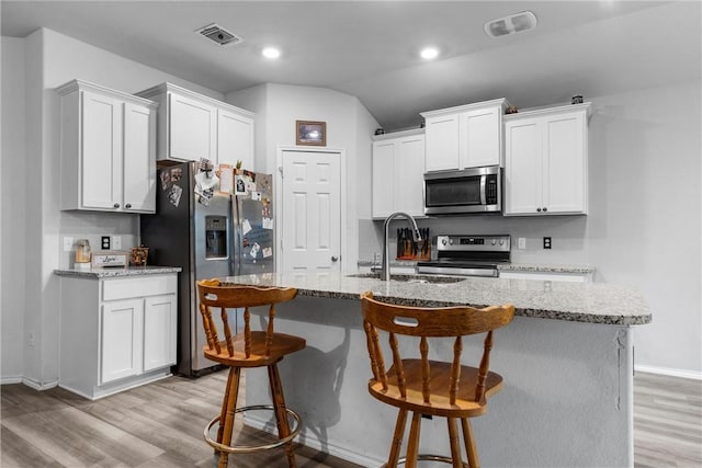 kitchen featuring appliances with stainless steel finishes, visible vents, light wood-style floors, and a kitchen breakfast bar