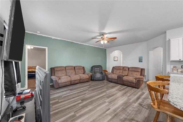 living area with arched walkways, light wood-type flooring, and a ceiling fan