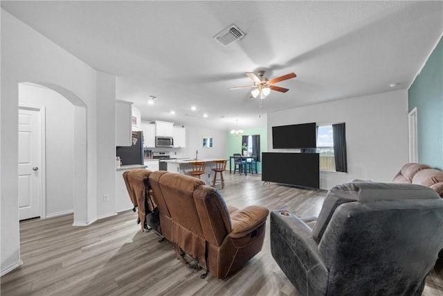 living area with light wood finished floors, visible vents, arched walkways, and a ceiling fan