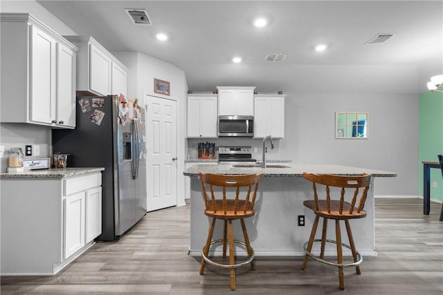 kitchen with light wood finished floors, visible vents, appliances with stainless steel finishes, a breakfast bar, and a sink