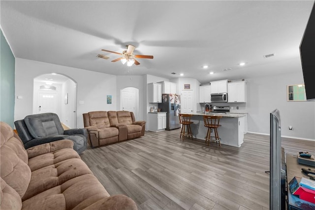 living room featuring arched walkways, recessed lighting, visible vents, light wood-style flooring, and a ceiling fan