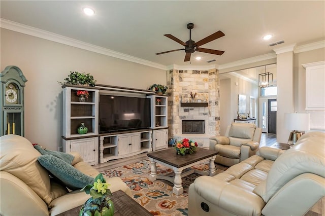 living room featuring a stone fireplace, crown molding, light hardwood / wood-style flooring, and ceiling fan with notable chandelier