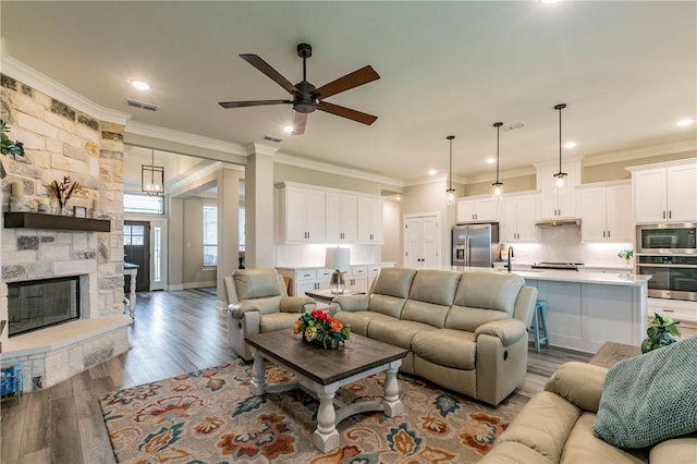 living room featuring ceiling fan, crown molding, sink, light hardwood / wood-style flooring, and a fireplace