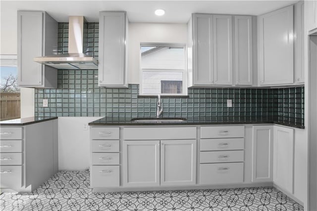 kitchen with sink, decorative backsplash, wall chimney range hood, and white cabinetry