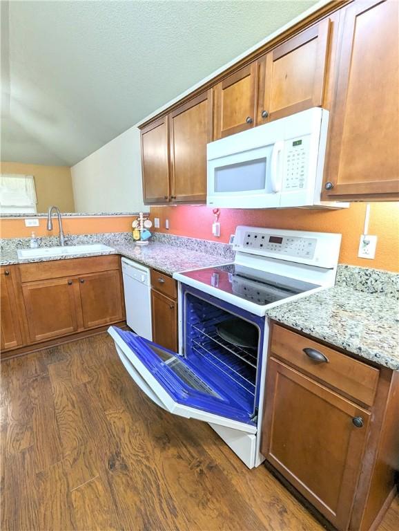 kitchen featuring dark hardwood / wood-style flooring, white appliances, light stone counters, and sink