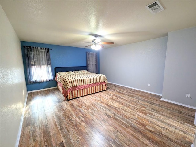 bedroom with ceiling fan, wood-type flooring, and a textured ceiling