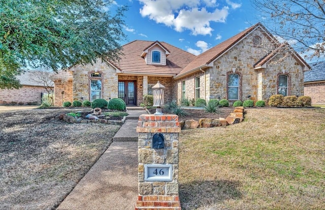 french country home with stone siding, french doors, and a front lawn