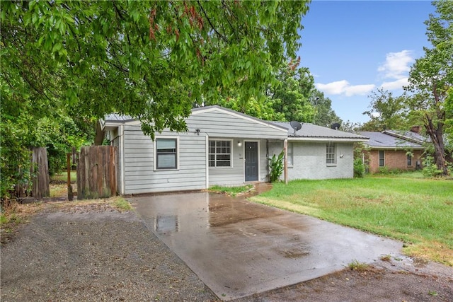 ranch-style home with concrete driveway, metal roof, fence, a front lawn, and brick siding