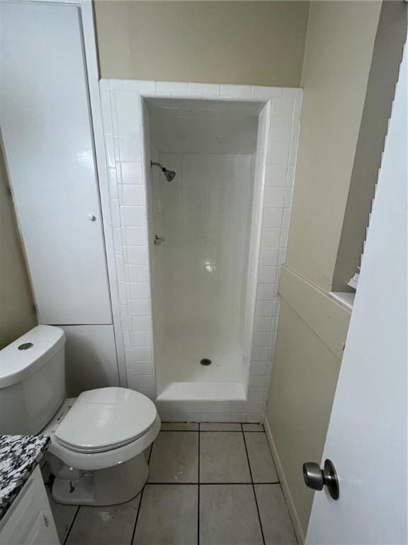 bathroom featuring tile patterned floors, toilet, vanity, and a tile shower