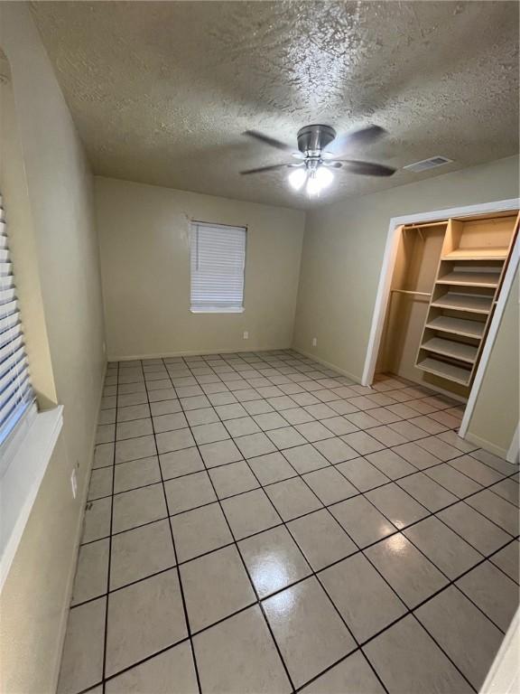 unfurnished bedroom with light tile patterned floors, a textured ceiling, and ceiling fan