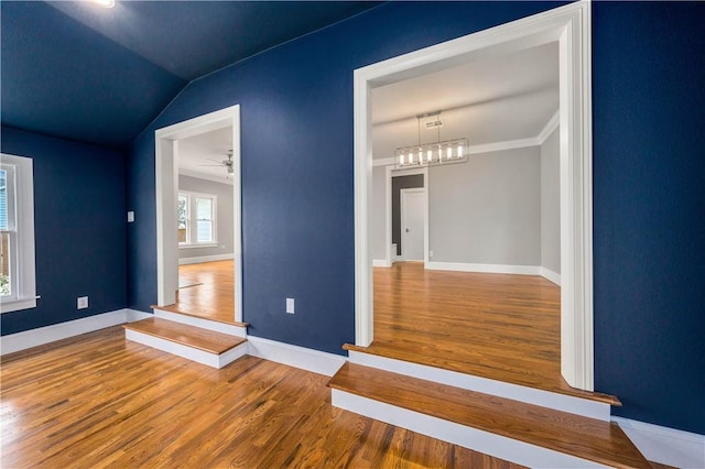 interior space featuring wood-type flooring, ceiling fan with notable chandelier, ornamental molding, and lofted ceiling