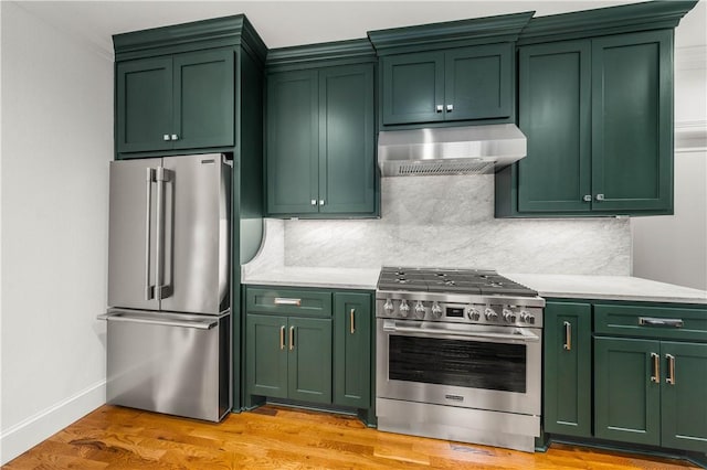 kitchen featuring exhaust hood, green cabinets, light wood-type flooring, appliances with stainless steel finishes, and tasteful backsplash