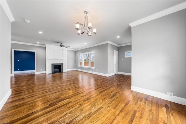 unfurnished living room with ceiling fan with notable chandelier, hardwood / wood-style floors, a large fireplace, and ornamental molding