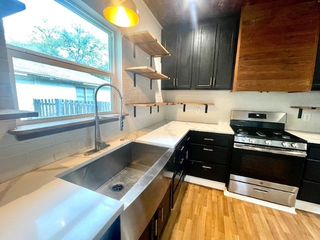 kitchen with open shelves, light wood-style flooring, a sink, gas range, and dark cabinetry