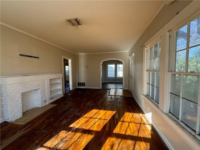 unfurnished living room with a brick fireplace, built in features, dark wood-type flooring, and ornamental molding