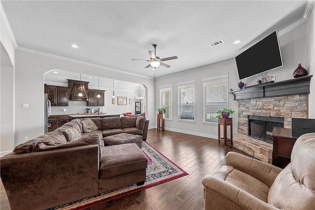 living room with hardwood / wood-style flooring, crown molding, a stone fireplace, and ceiling fan