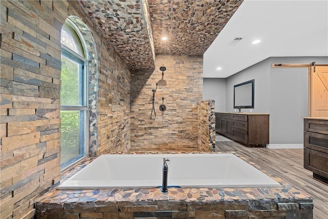 bathroom with hardwood / wood-style flooring, vanity, and tiled bath