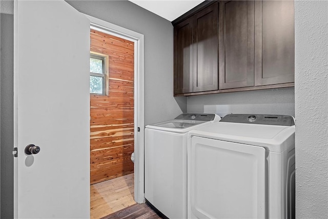 laundry area featuring hardwood / wood-style floors, cabinets, wooden walls, and washing machine and clothes dryer