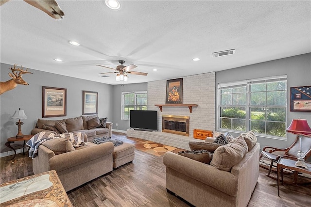 living room featuring hardwood / wood-style flooring, ceiling fan, a textured ceiling, and a brick fireplace