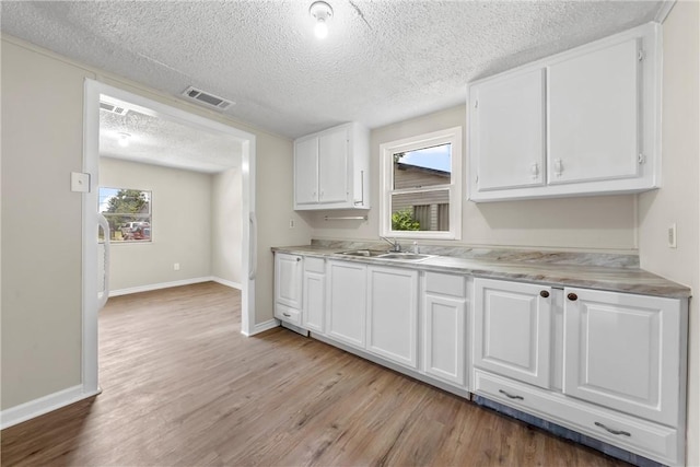 kitchen featuring white cabinets, a textured ceiling, sink, and light hardwood / wood-style flooring