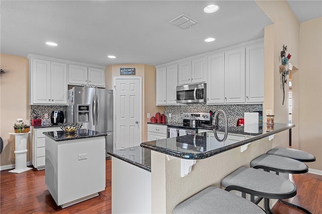 kitchen featuring kitchen peninsula, appliances with stainless steel finishes, dark hardwood / wood-style floors, and white cabinetry