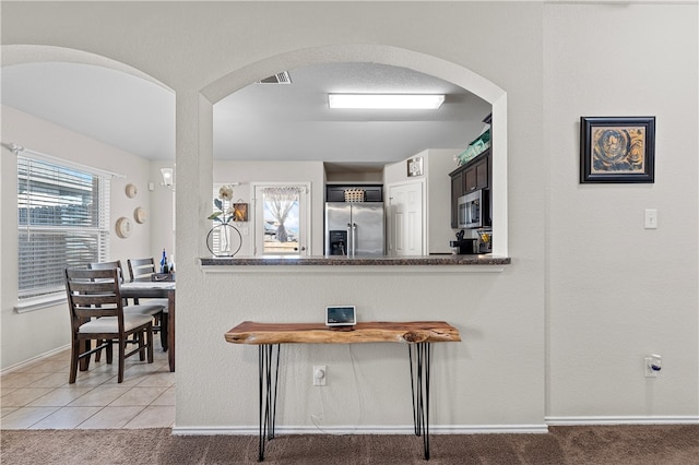 kitchen with dark brown cabinets, light colored carpet, kitchen peninsula, and stainless steel appliances