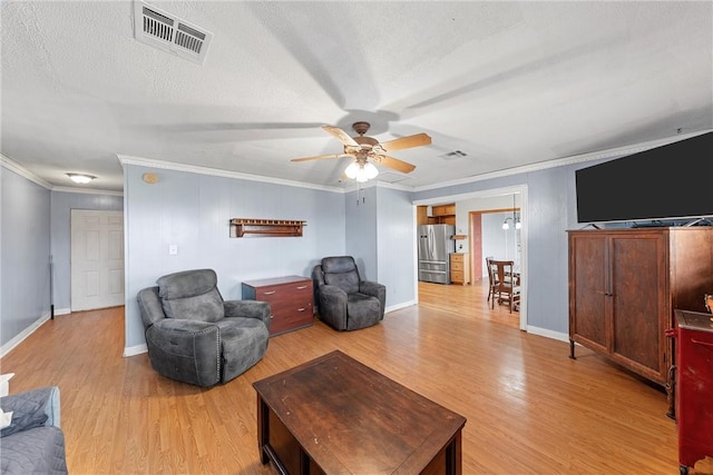 living area featuring light wood-style floors, visible vents, ornamental molding, and a textured ceiling