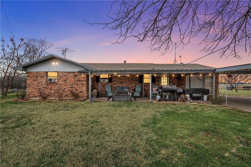 back of house at dusk with a patio area, a yard, and brick siding