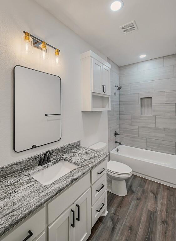 full bathroom with hardwood / wood-style floors, vanity, toilet, and tiled shower / bath