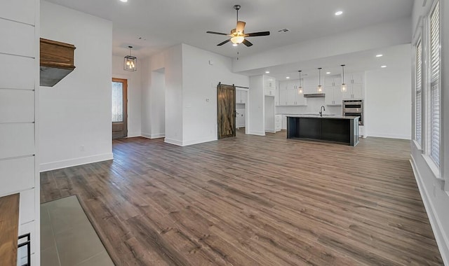 unfurnished living room with a barn door, ceiling fan, dark hardwood / wood-style flooring, and sink