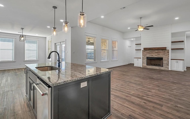 kitchen featuring pendant lighting, a kitchen island with sink, sink, light stone countertops, and a fireplace