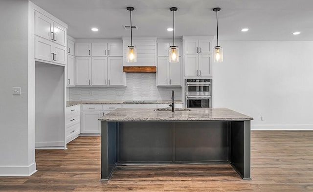 kitchen featuring dark wood-type flooring, white cabinets, an island with sink, and decorative light fixtures