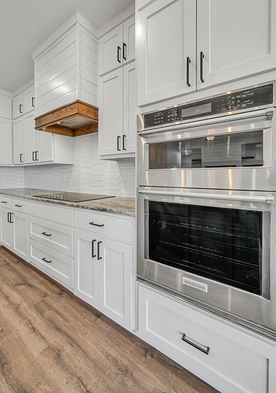 kitchen featuring black electric stovetop, wood-type flooring, stainless steel double oven, light stone countertops, and white cabinetry