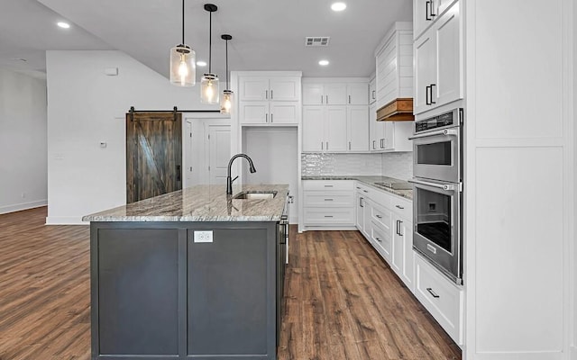 kitchen featuring sink, a barn door, white cabinetry, and an island with sink