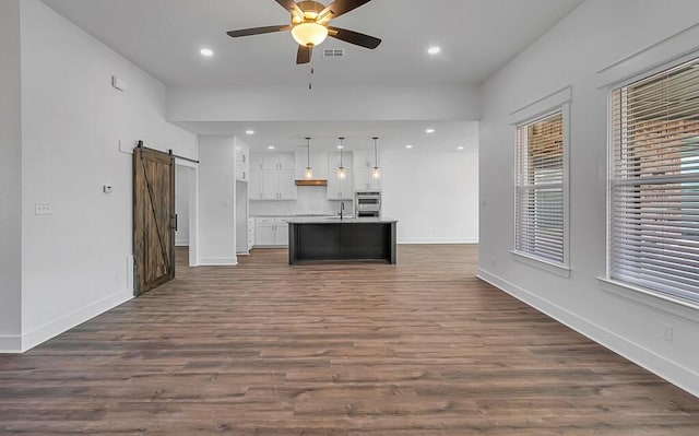 unfurnished living room with a barn door, ceiling fan, sink, and dark hardwood / wood-style floors