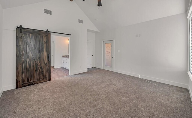 unfurnished bedroom featuring carpet flooring, ensuite bathroom, ceiling fan, a barn door, and high vaulted ceiling