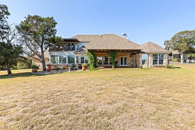 rear view of property featuring french doors, a balcony, and a lawn