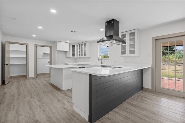 kitchen featuring light hardwood / wood-style floors, white cabinetry, kitchen peninsula, and island exhaust hood