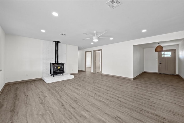 unfurnished living room with a wood stove, ceiling fan, and hardwood / wood-style floors