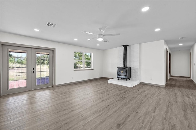 unfurnished living room featuring hardwood / wood-style flooring, ceiling fan, a wood stove, and french doors