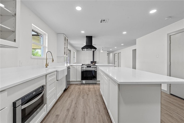 kitchen featuring white cabinetry, ventilation hood, light wood-type flooring, and appliances with stainless steel finishes