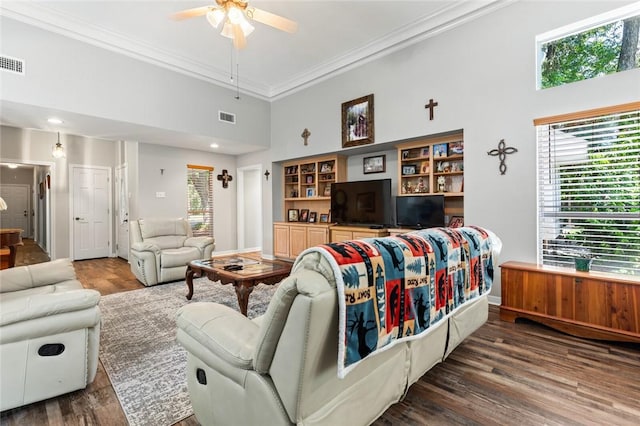 living room featuring ceiling fan, a towering ceiling, dark hardwood / wood-style floors, ornamental molding, and built in shelves