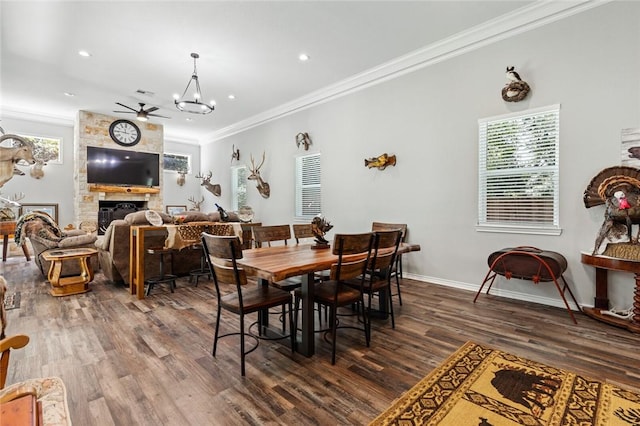 dining area with ornamental molding, a stone fireplace, dark hardwood / wood-style floors, and ceiling fan with notable chandelier