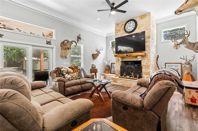 living room featuring hardwood / wood-style flooring, crown molding, a stone fireplace, and ceiling fan