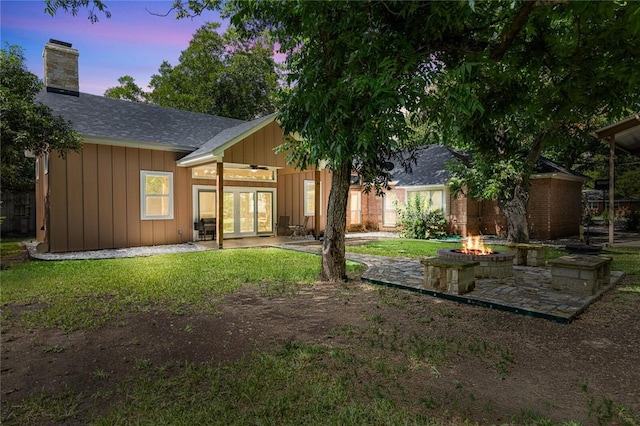 back house at dusk with french doors, a yard, a patio, and an outdoor fire pit