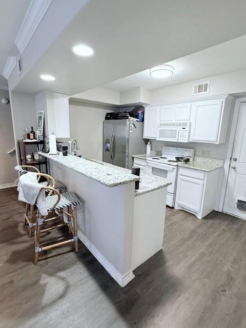 kitchen featuring white appliances, dark wood-type flooring, light stone counters, white cabinets, and kitchen peninsula