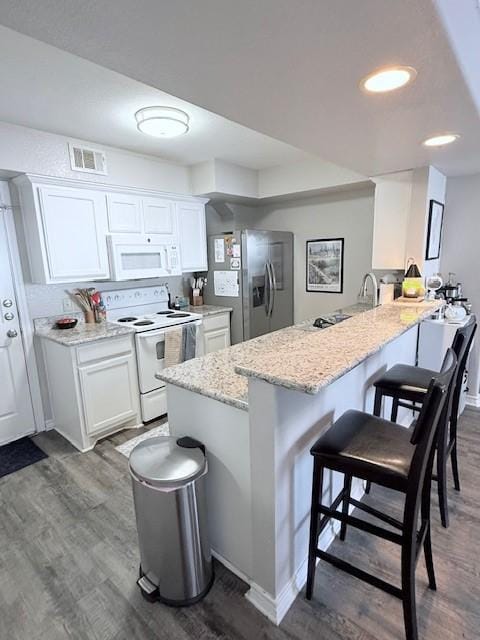 kitchen featuring dark wood-type flooring, a breakfast bar, white cabinetry, white appliances, and light stone countertops