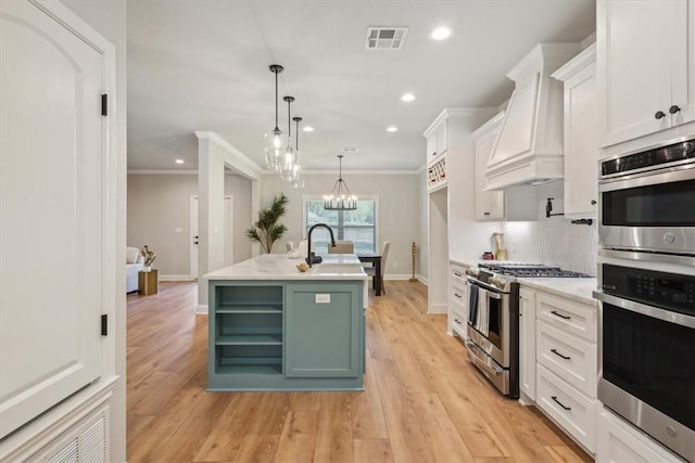 kitchen with white cabinets, appliances with stainless steel finishes, a center island with sink, and light hardwood / wood-style floors