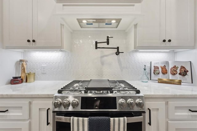 kitchen with decorative backsplash, stainless steel gas range oven, light stone counters, and white cabinetry