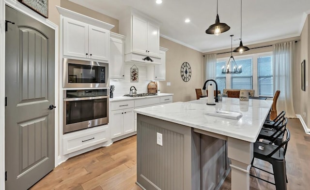 kitchen with pendant lighting, white cabinetry, a kitchen island with sink, stainless steel appliances, and light stone countertops